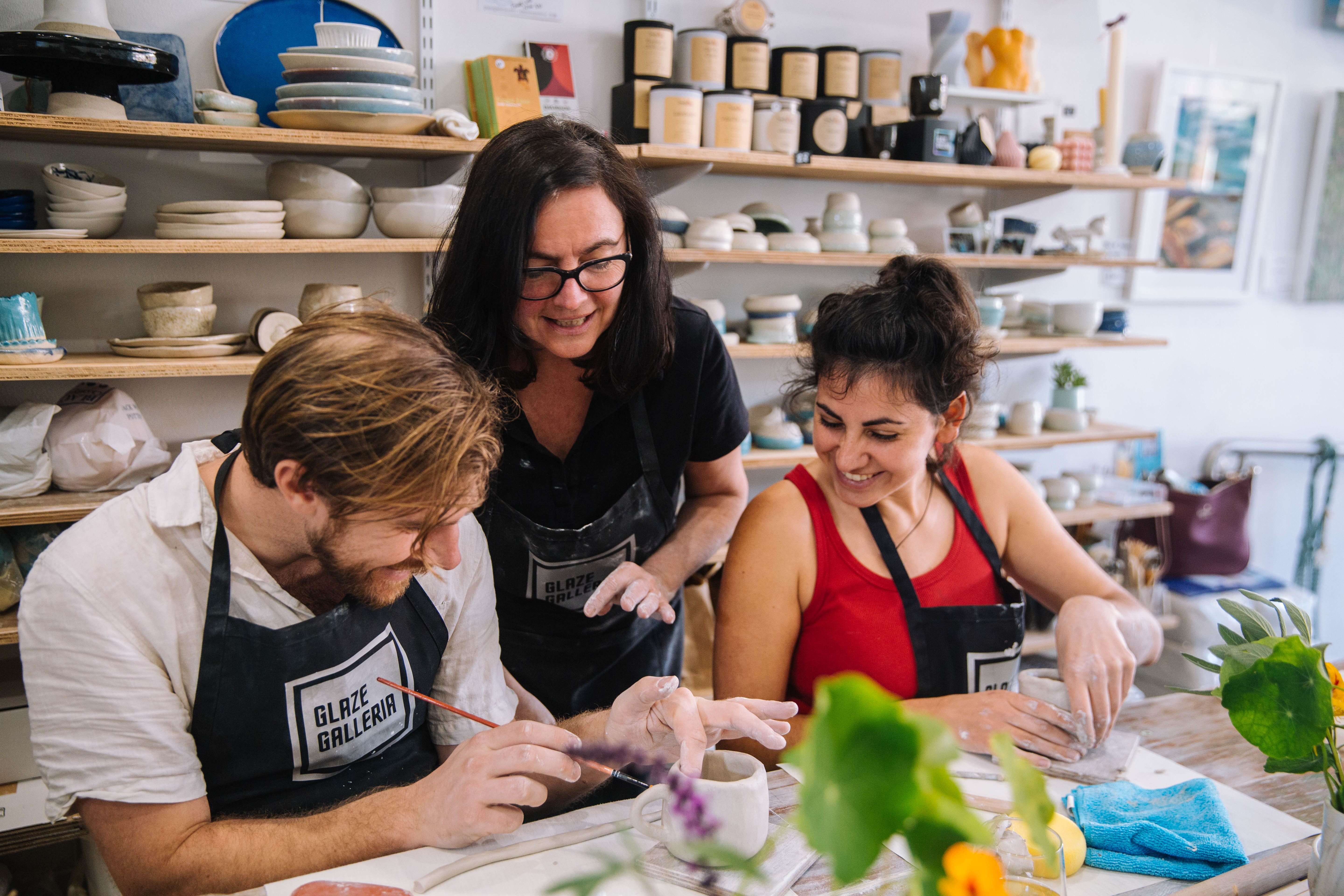 A teacher helping two students at a pottery class